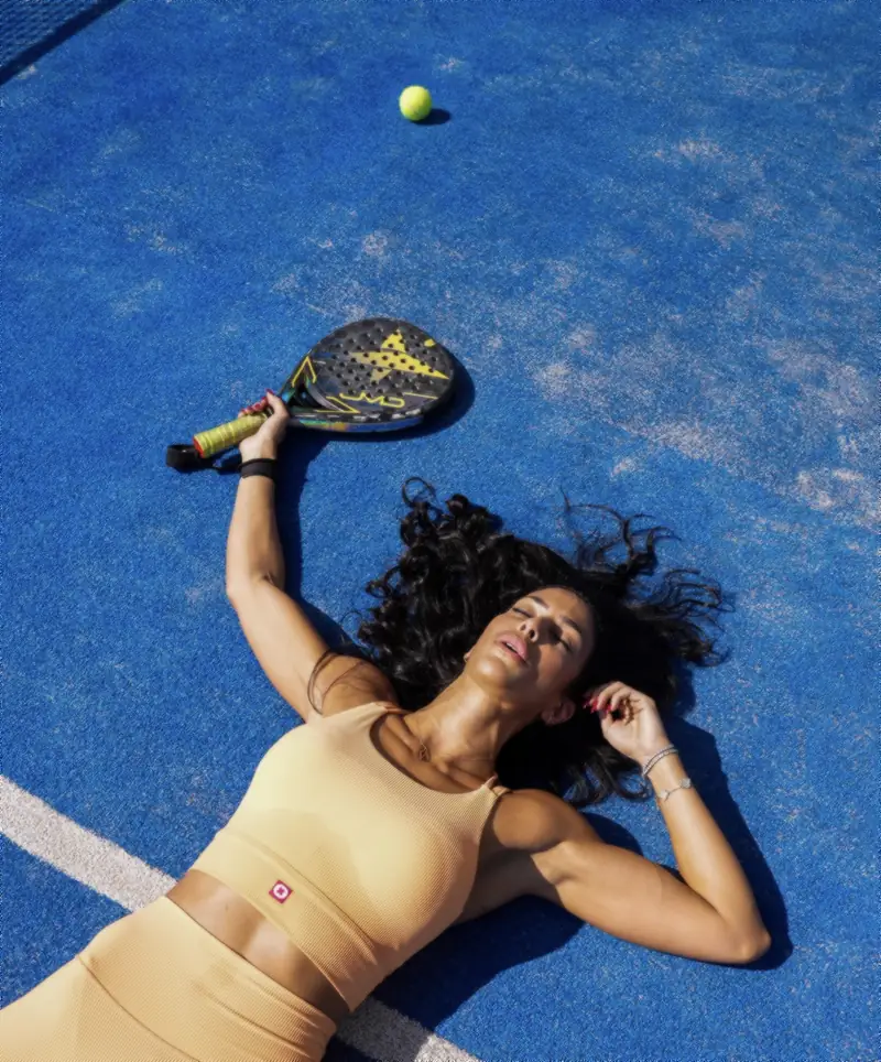 Padel player lying on a blue court with her racket and ball